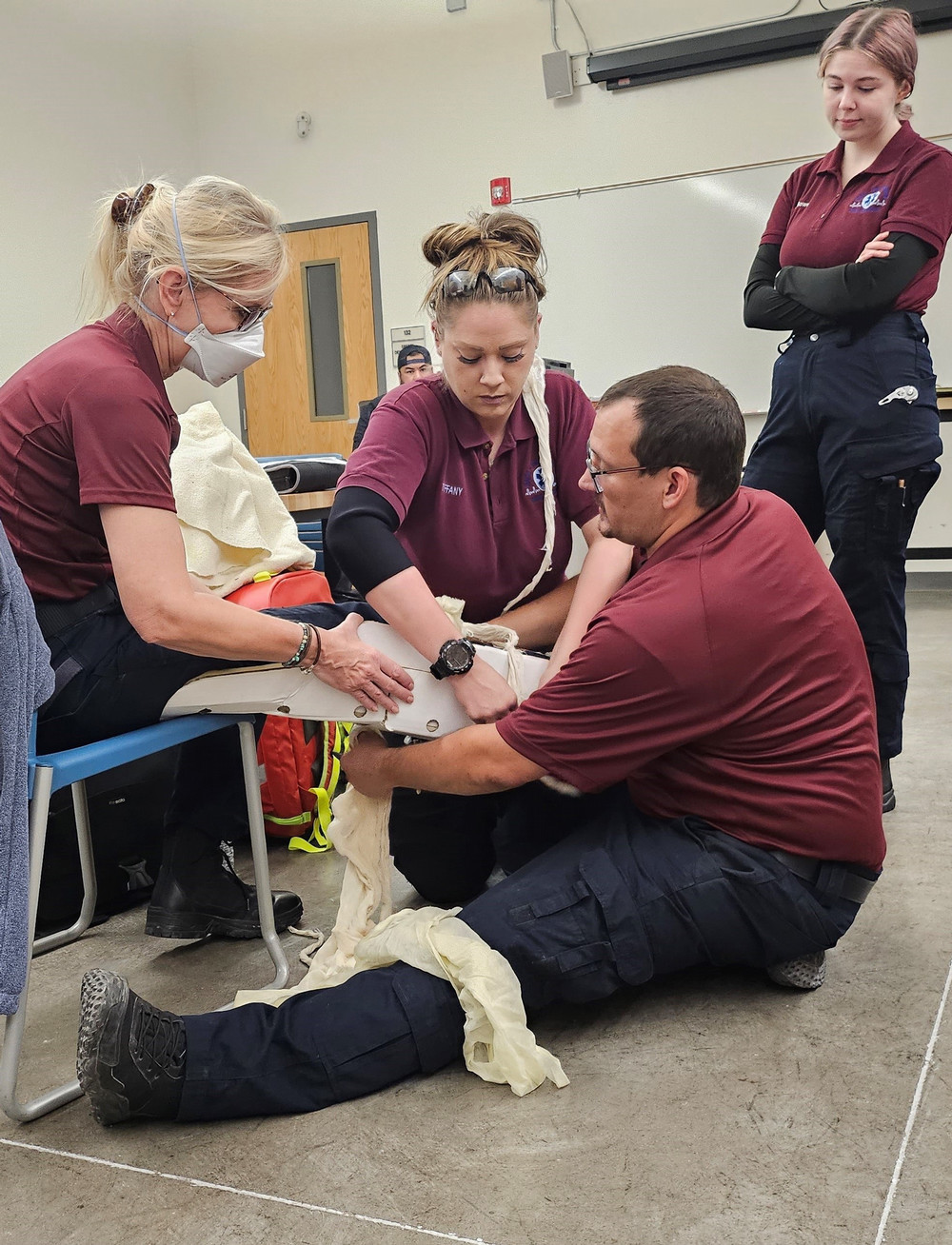 Trainees in EMS practice setting up a leg splint under instructor supervision.
